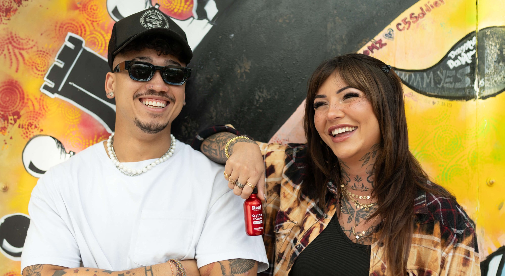Two people standing in front of a colorful graffiti wall.