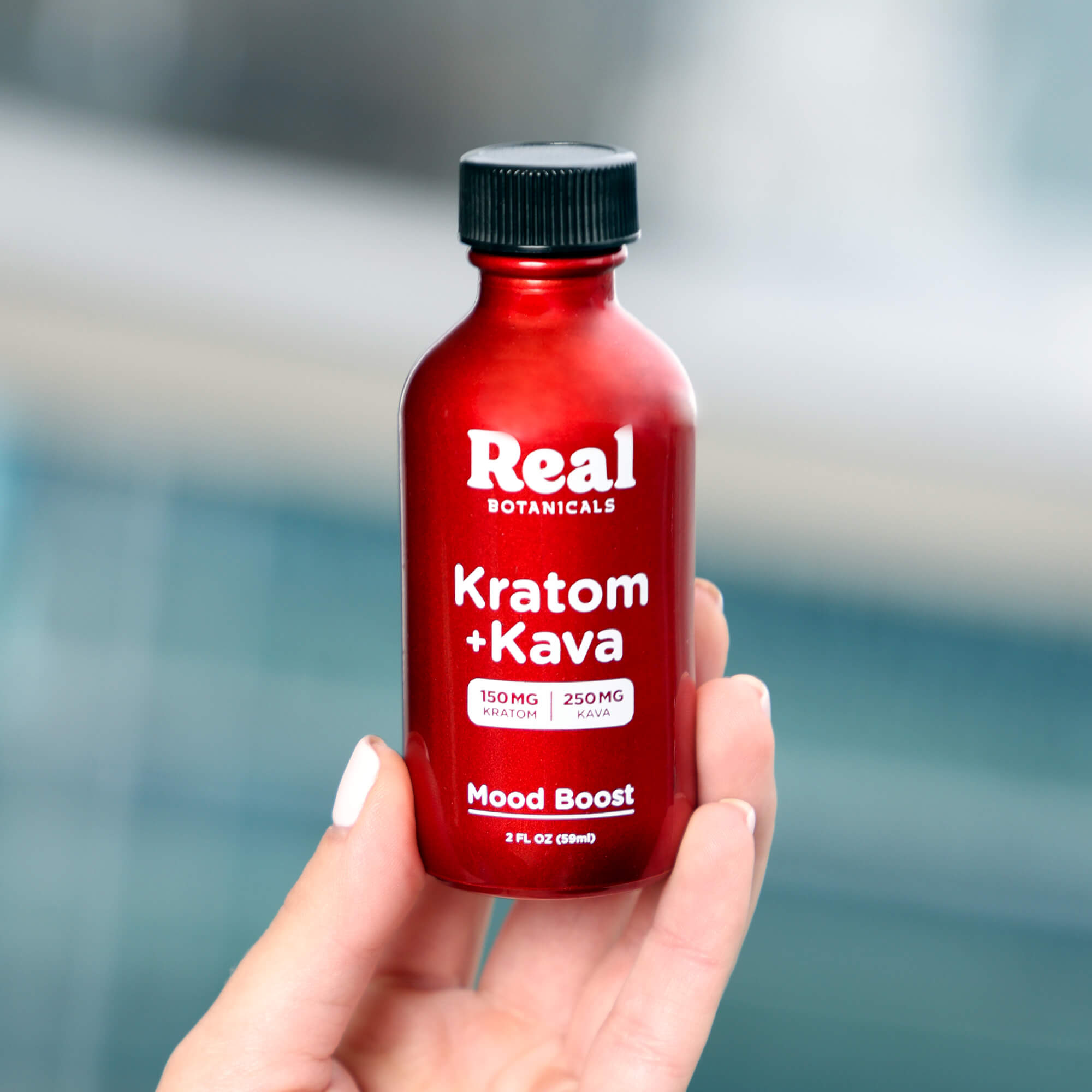 Red bottle labeled 'Real Botanicals Kratom + Kava' held by a hand with a blurred background