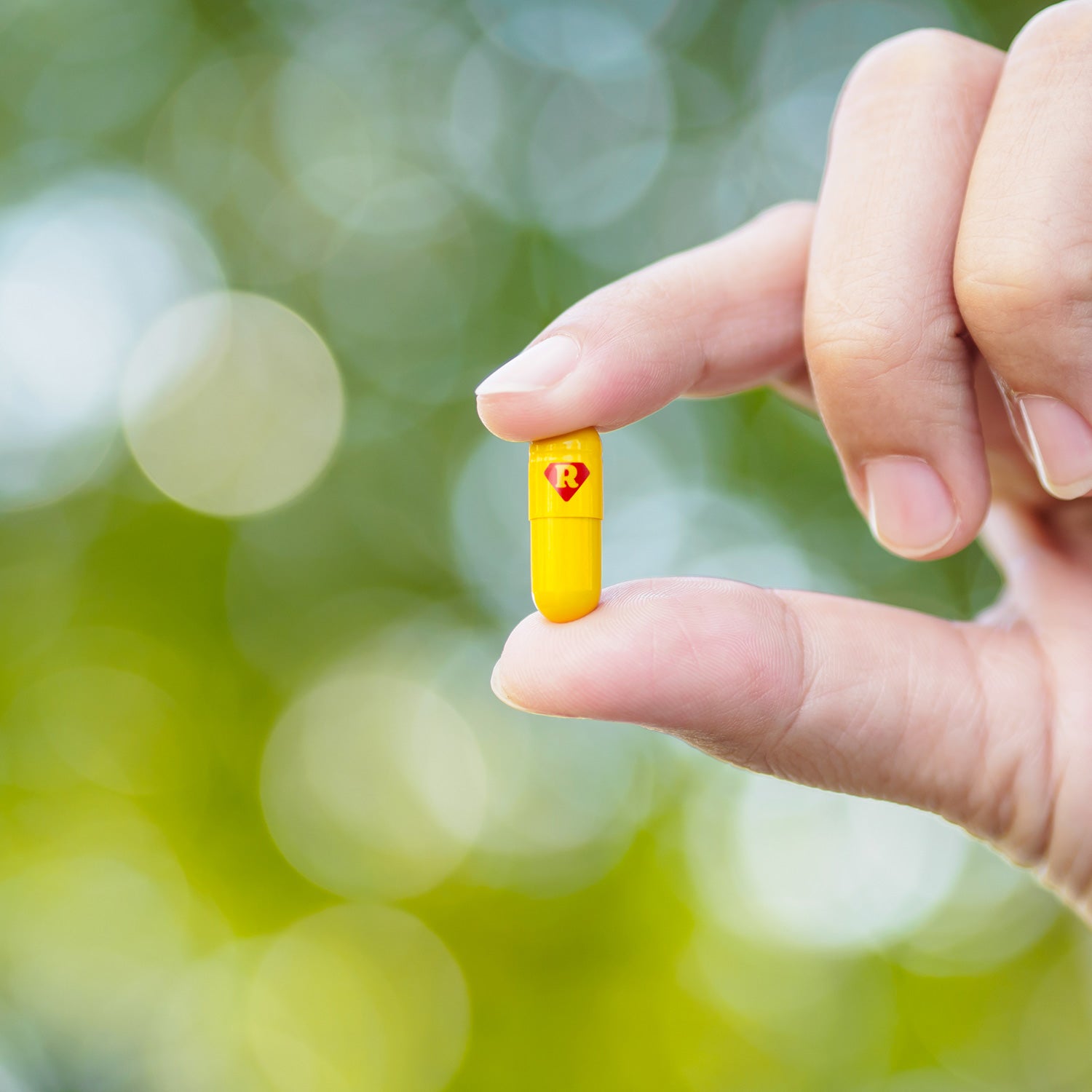 A hand holding a yellow pill with the letter R engraved on it