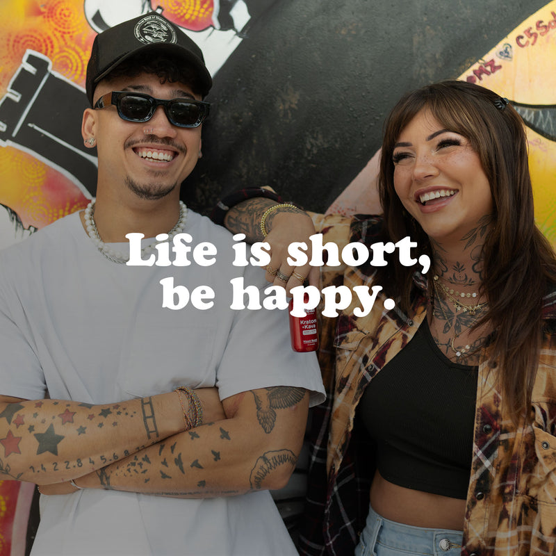 Smiling young man and woman with tattoos standing outdoors against graffiti wall, with the text 'Life is short, be happy' written across the image