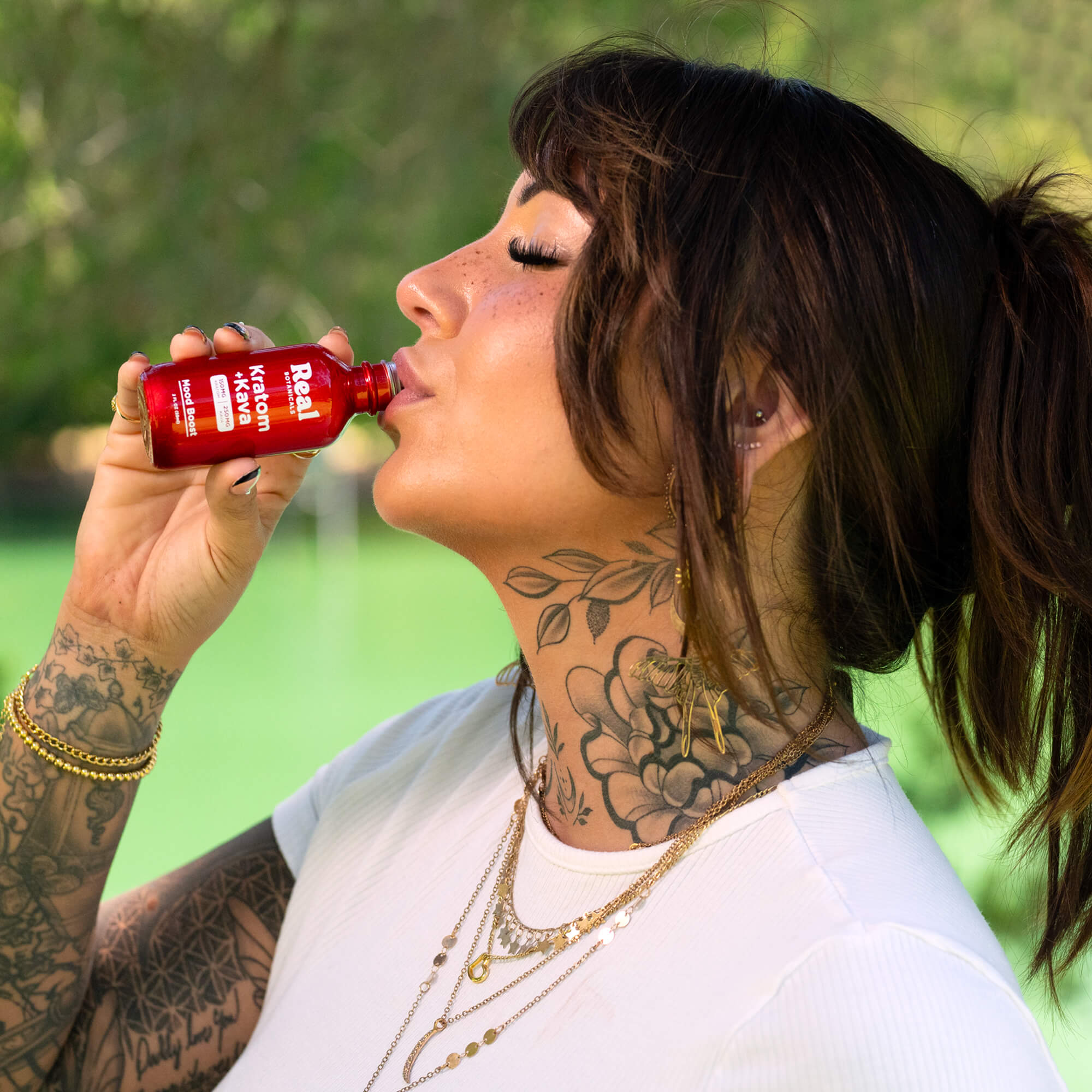 Woman drinking from a red bottle with a blurred green background