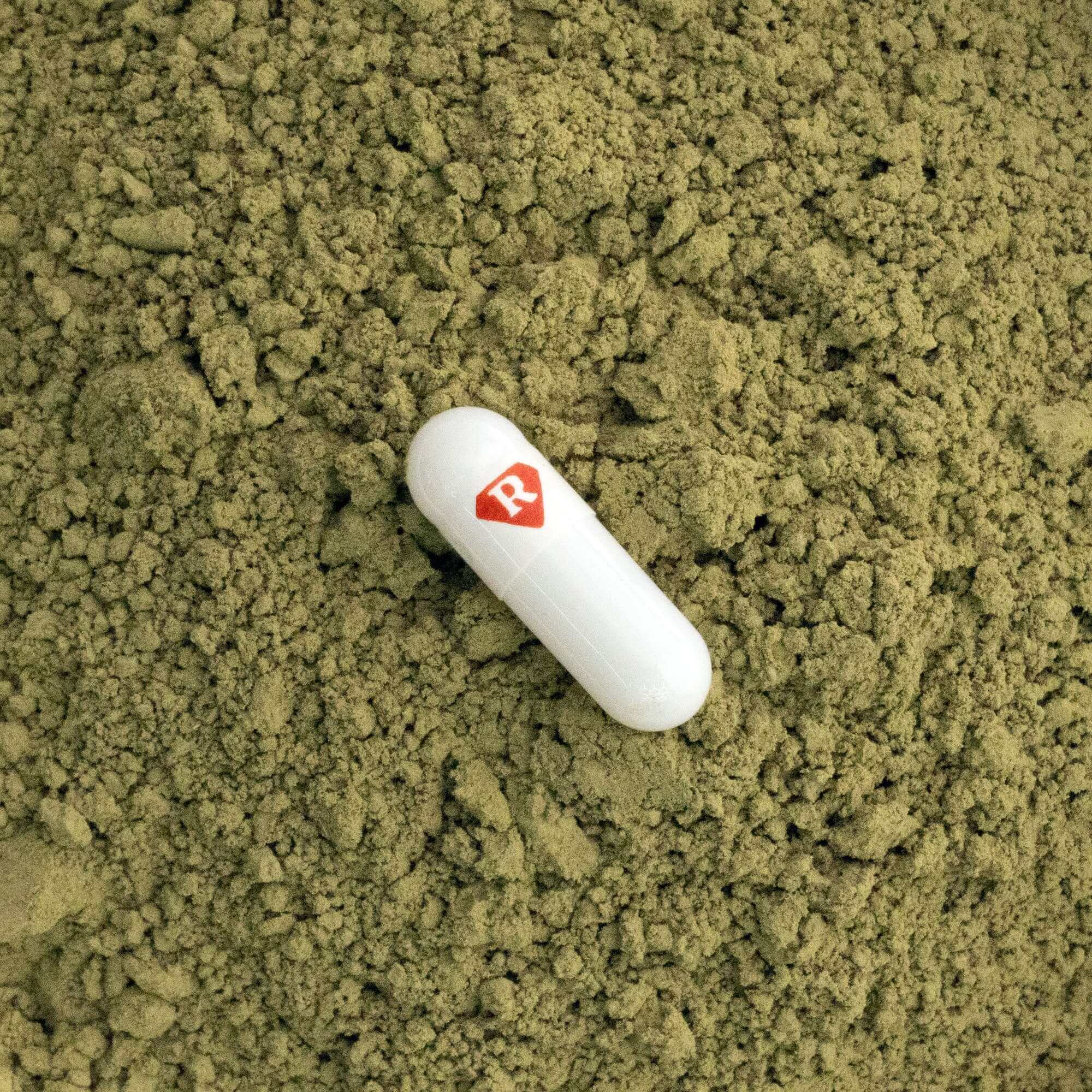 Kratom capsule on top of kratom powder