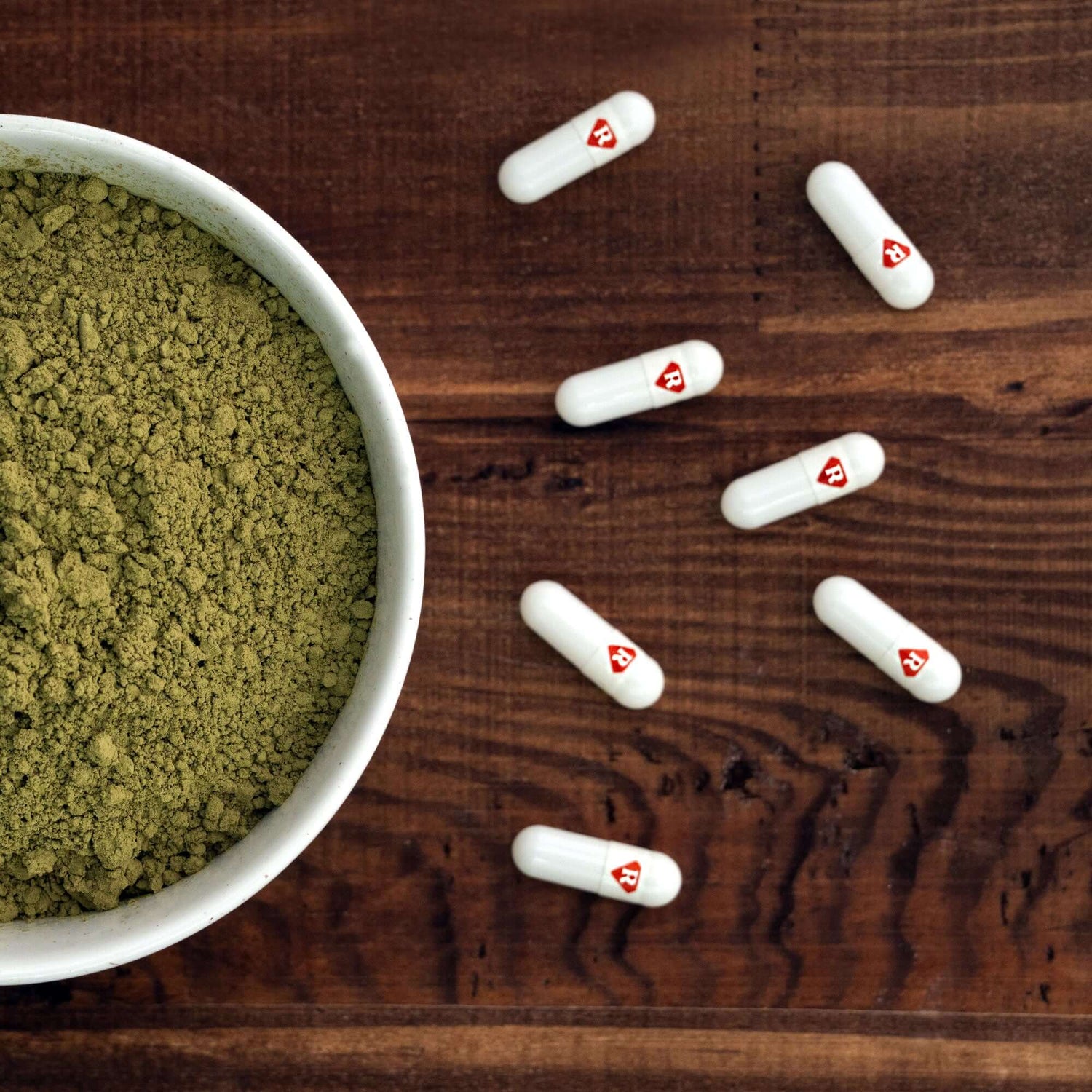 Kratom capsules spread out next to kratom powder